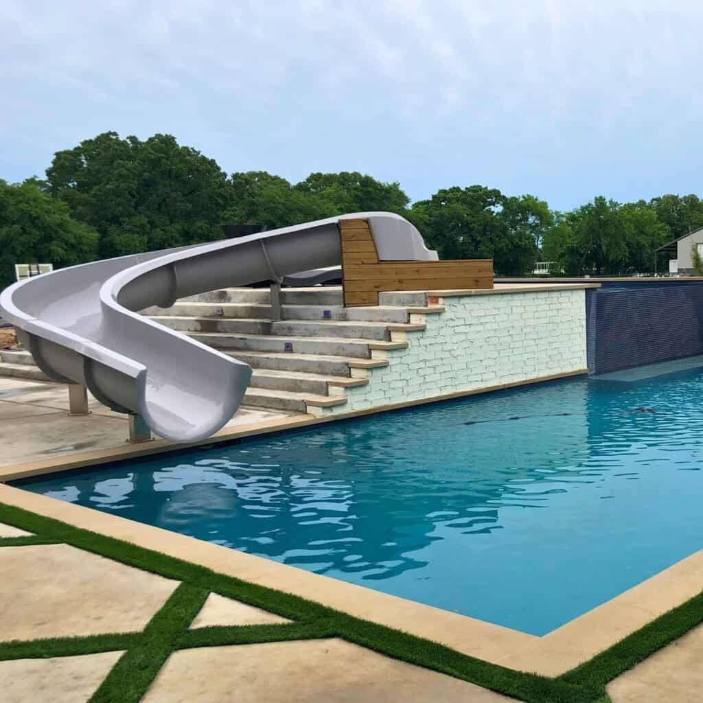 Vibrant outdoor pool with a sleek white slide and custom-designed steps for safety. Perfect for backyard recreation.